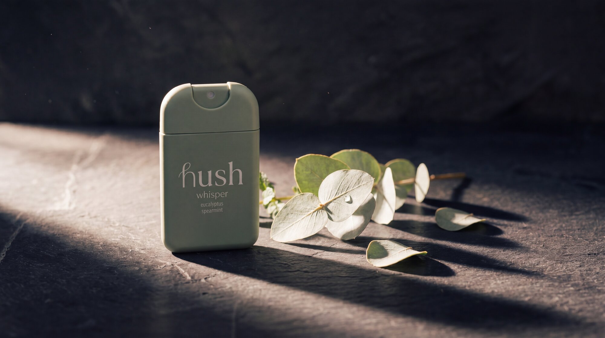 Hush Whisper with eucalyptus on dark stone in warm side light